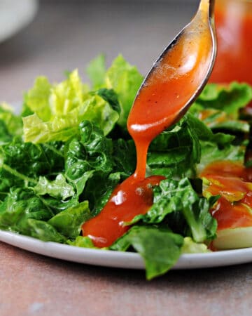 spoon of sweet catalina dressing pouring onto a green salad.