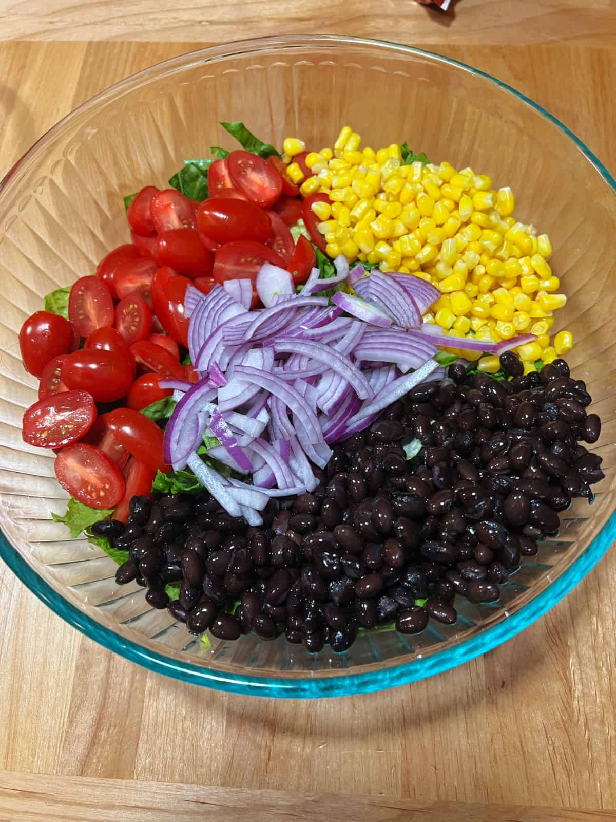 ingredients in a big bowl: lettuce, tomatoes, corn, black beans, red onion.