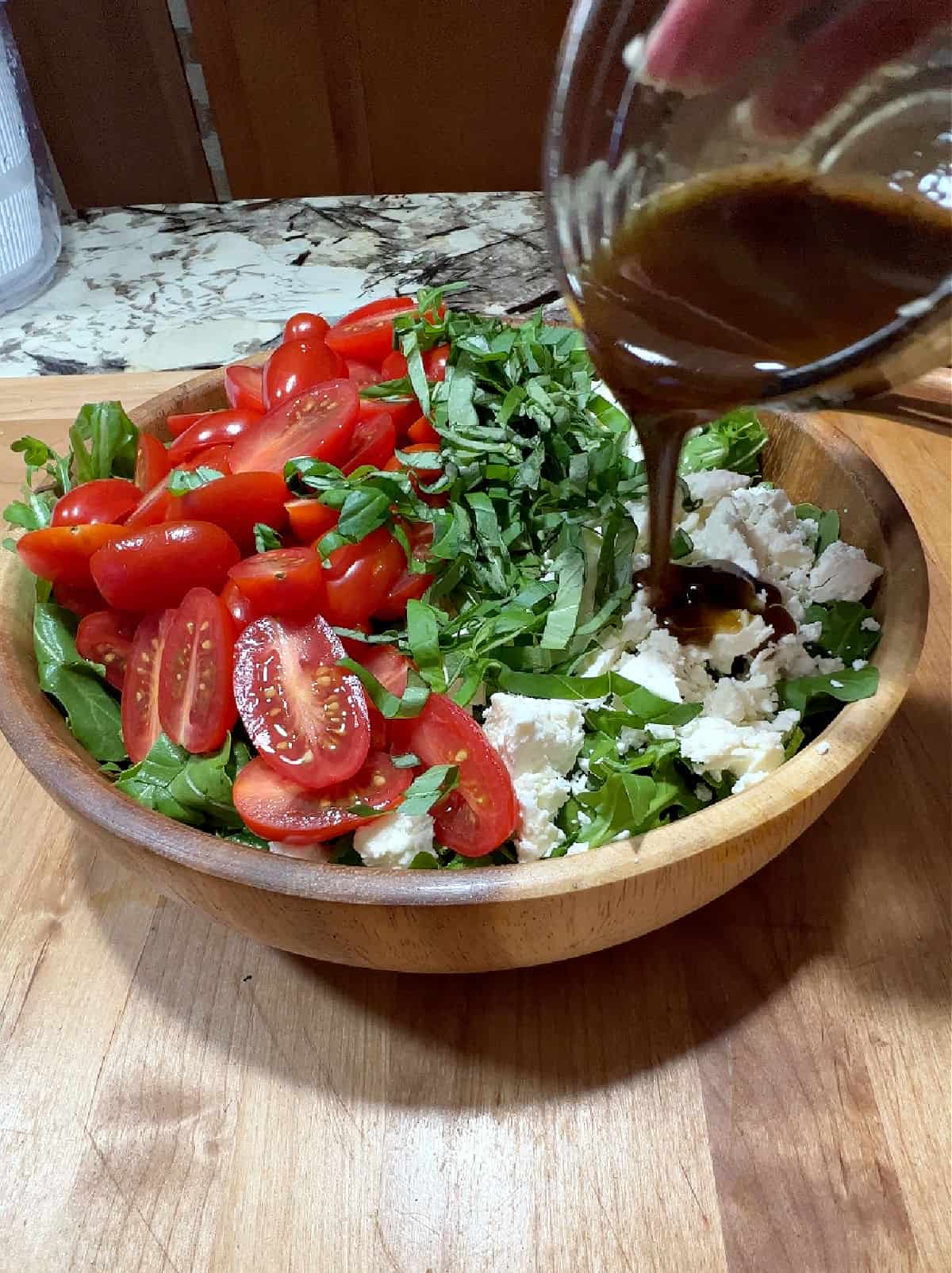 small cup of balsamic dressing pouring onto the salad.