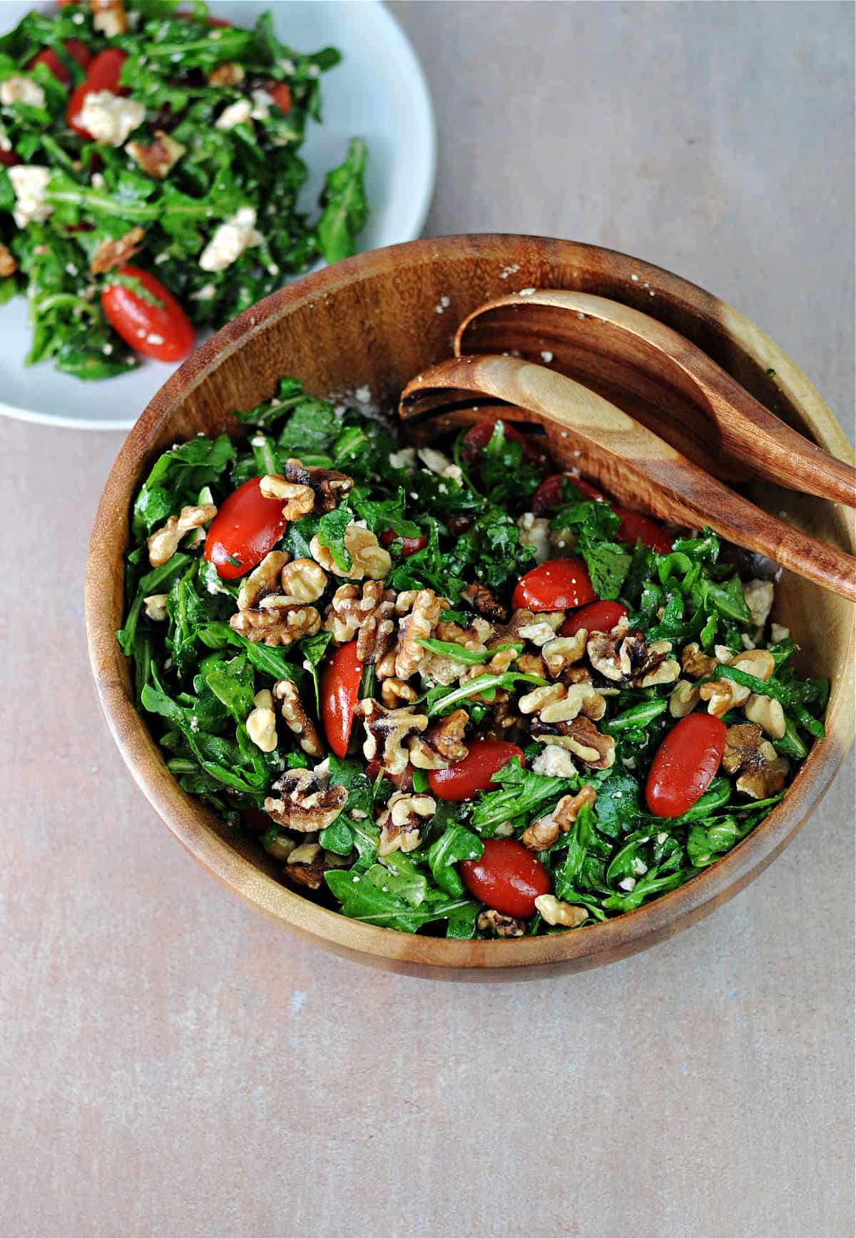 wood serving bowl filled with arugula feta tomato salad.