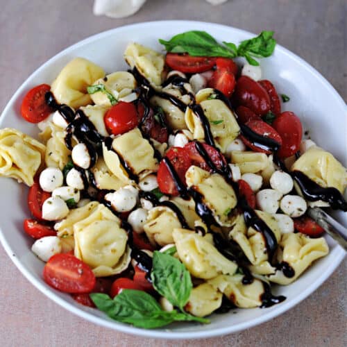serving bowl of caprese tortellini salad drizzled with balsamic glaze.