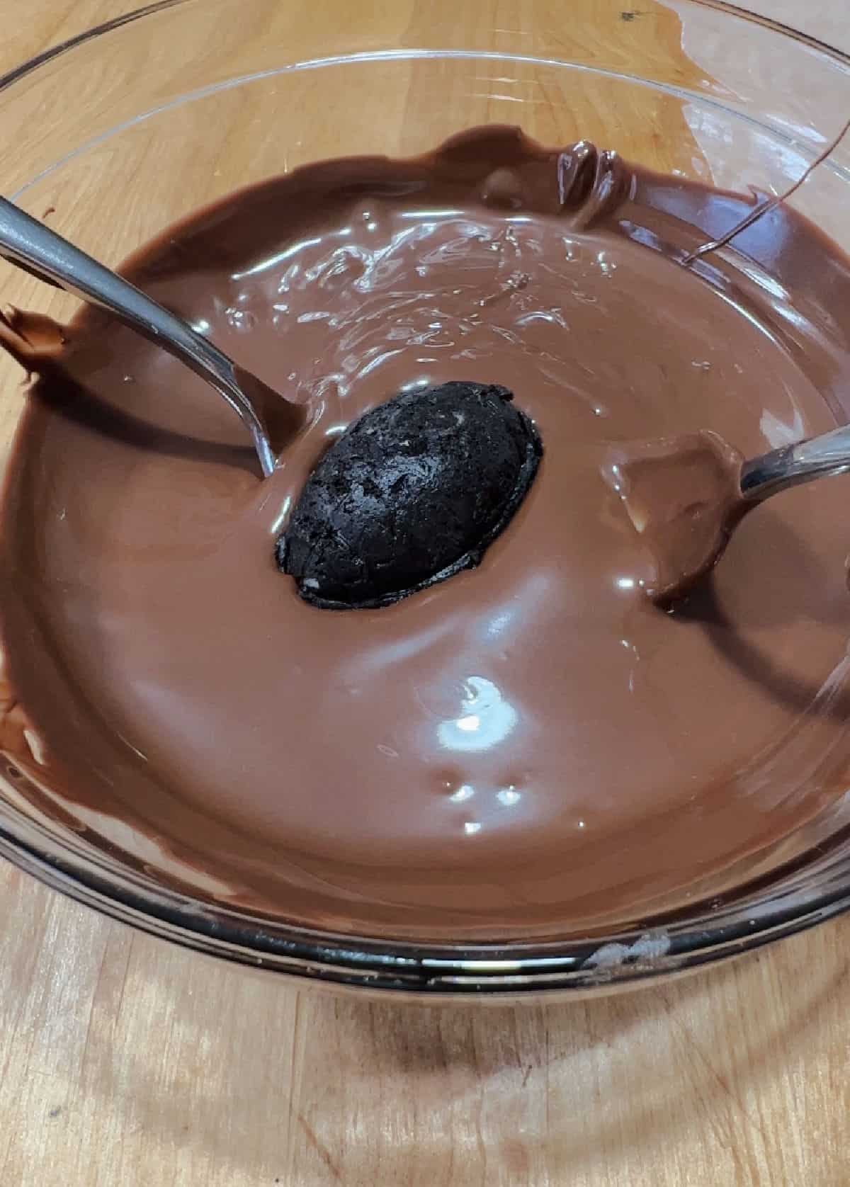 Oreo footbqall truffle placed in the bowl of melted chocolate coating.