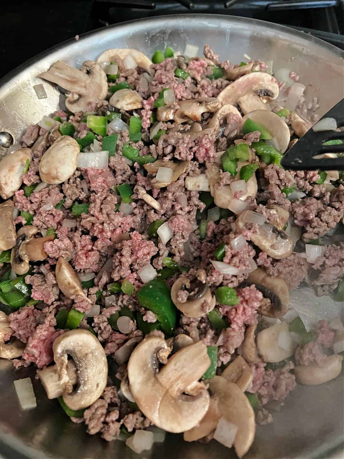 meat, green pepper, onion. and mushrooms cooking in a skillet.