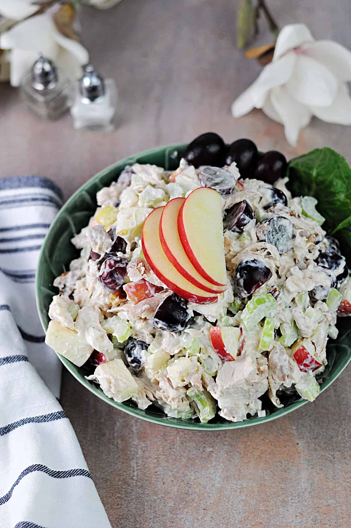 serving bowl of chicken waldorf salad garnished with grapes and apple slices.