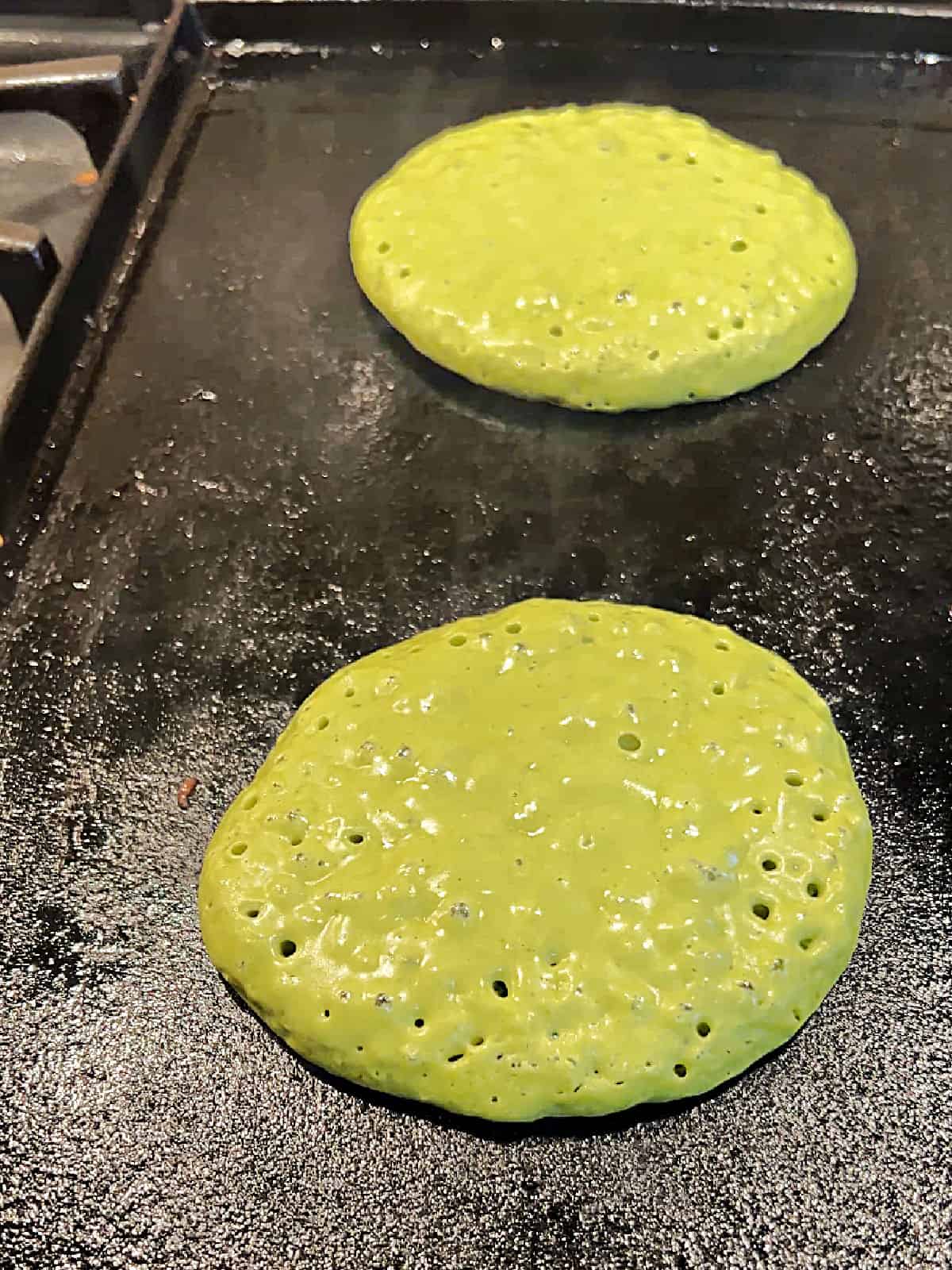 green matcha pancakes cooking on a cast iron griddle.