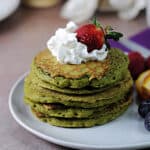 stack of matcha pancakes garnished with whipped cream and a strawberry.