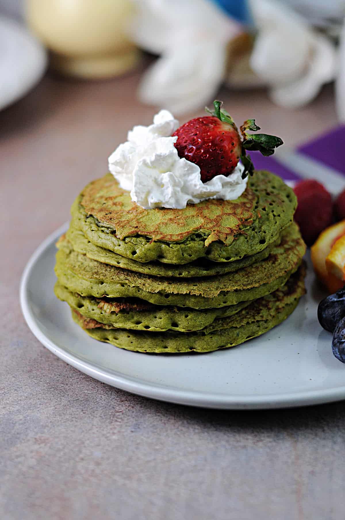 stack of matcha pancakes garnished with whipped cream and a strawberry.