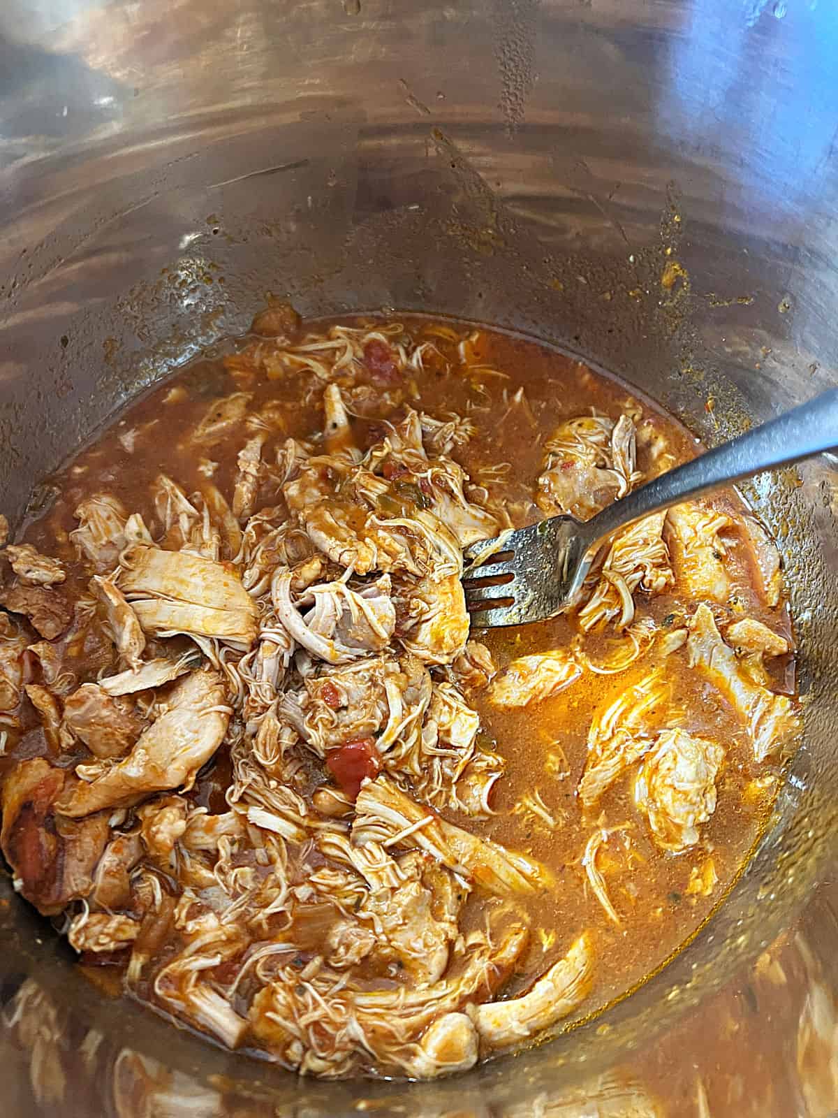 fork in the pot stirring to break up and shred the cooked chicken.