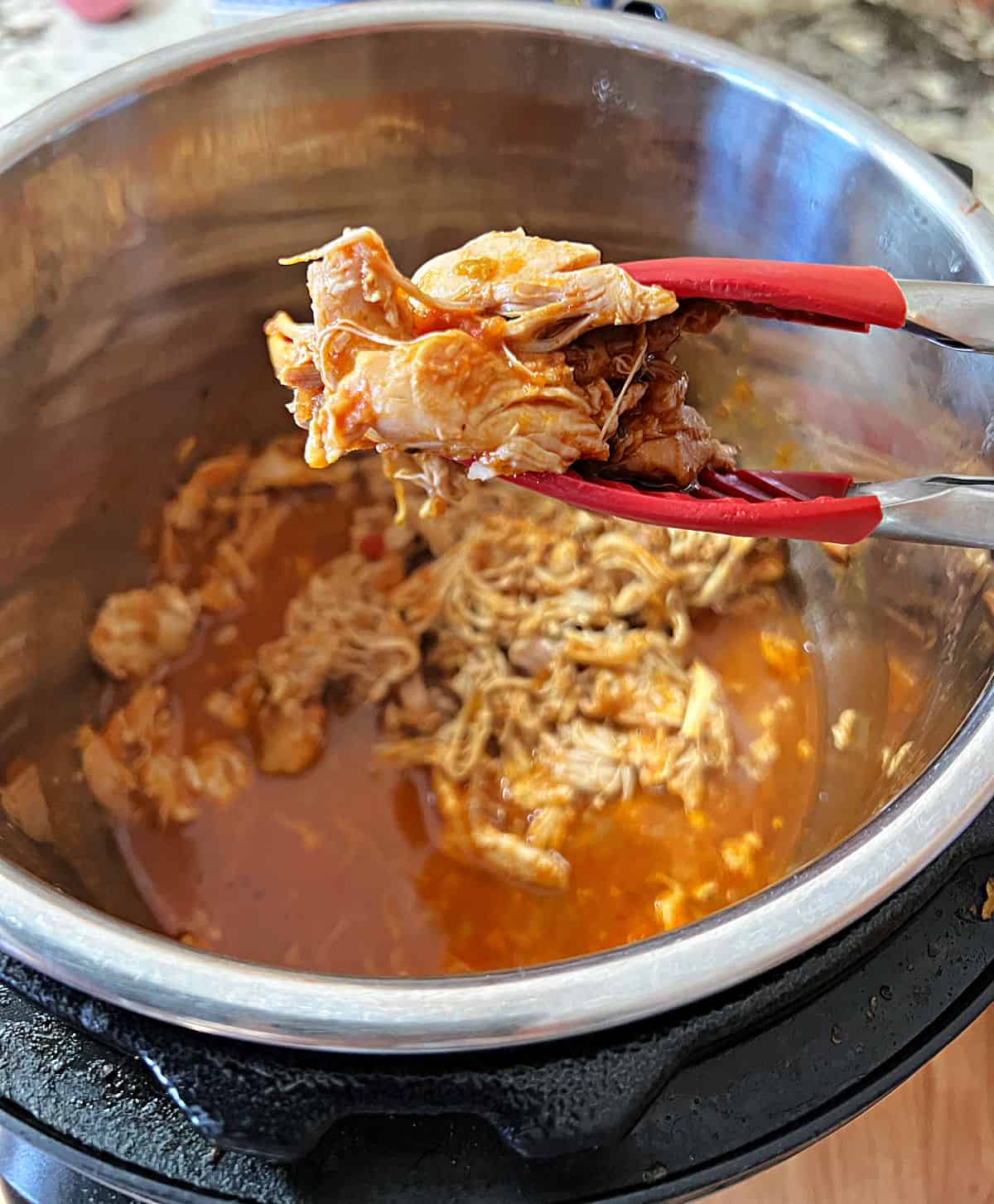 a tongs holding shredded salsa chicken over the instant pot full of more meat.