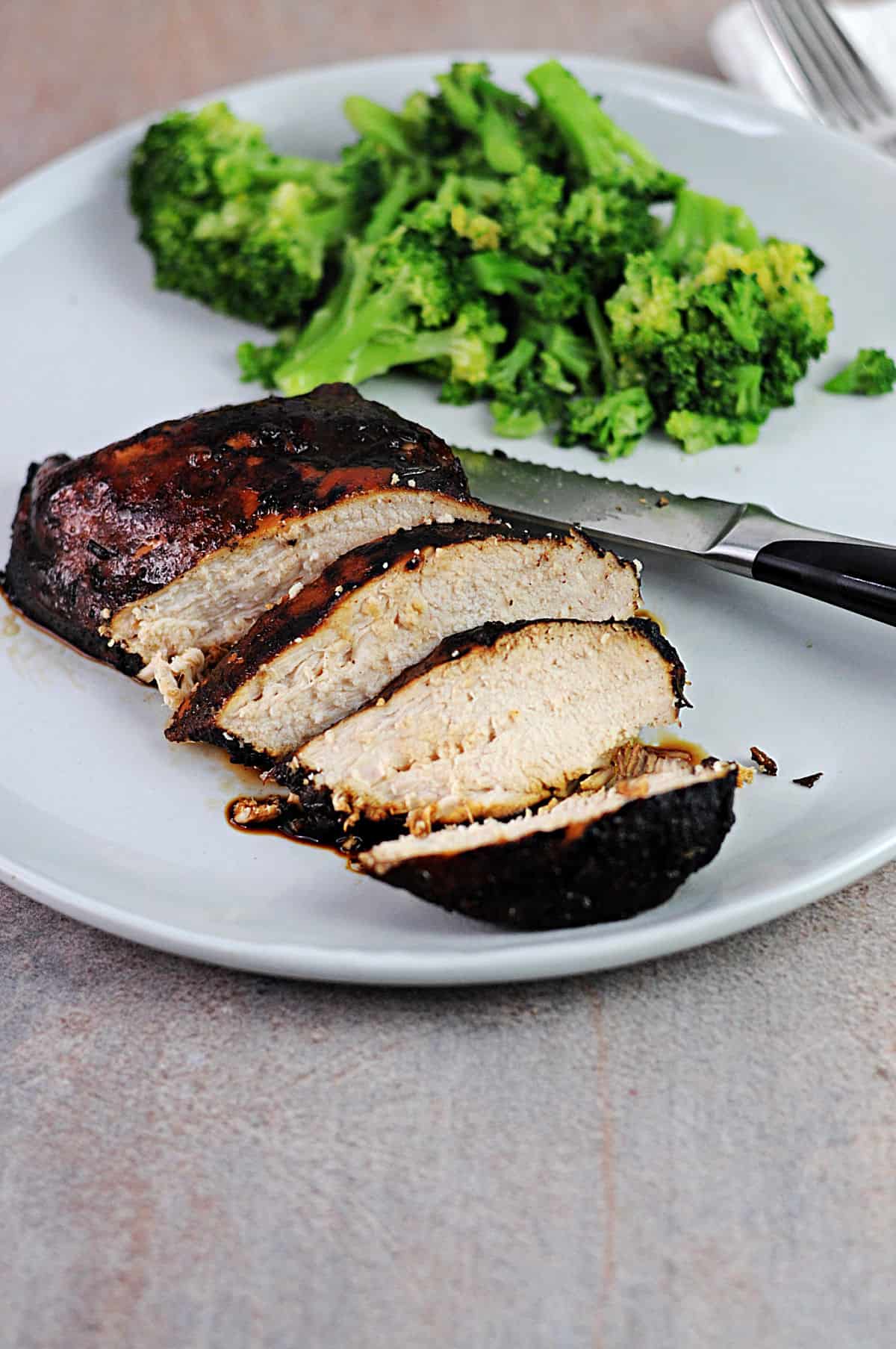 balsamic rosemary chicken breast sliced on a plate with some broccoli.