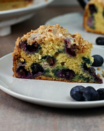slice of blueberry sour cream coffee cake on a plate, ready to eat.