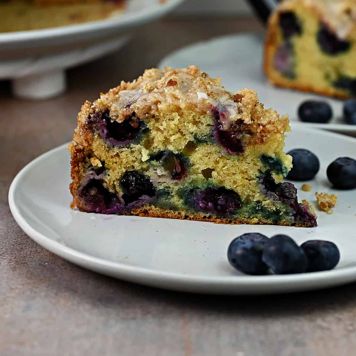 slice of blueberry sour cream coffee cake on a plate, ready to eat.