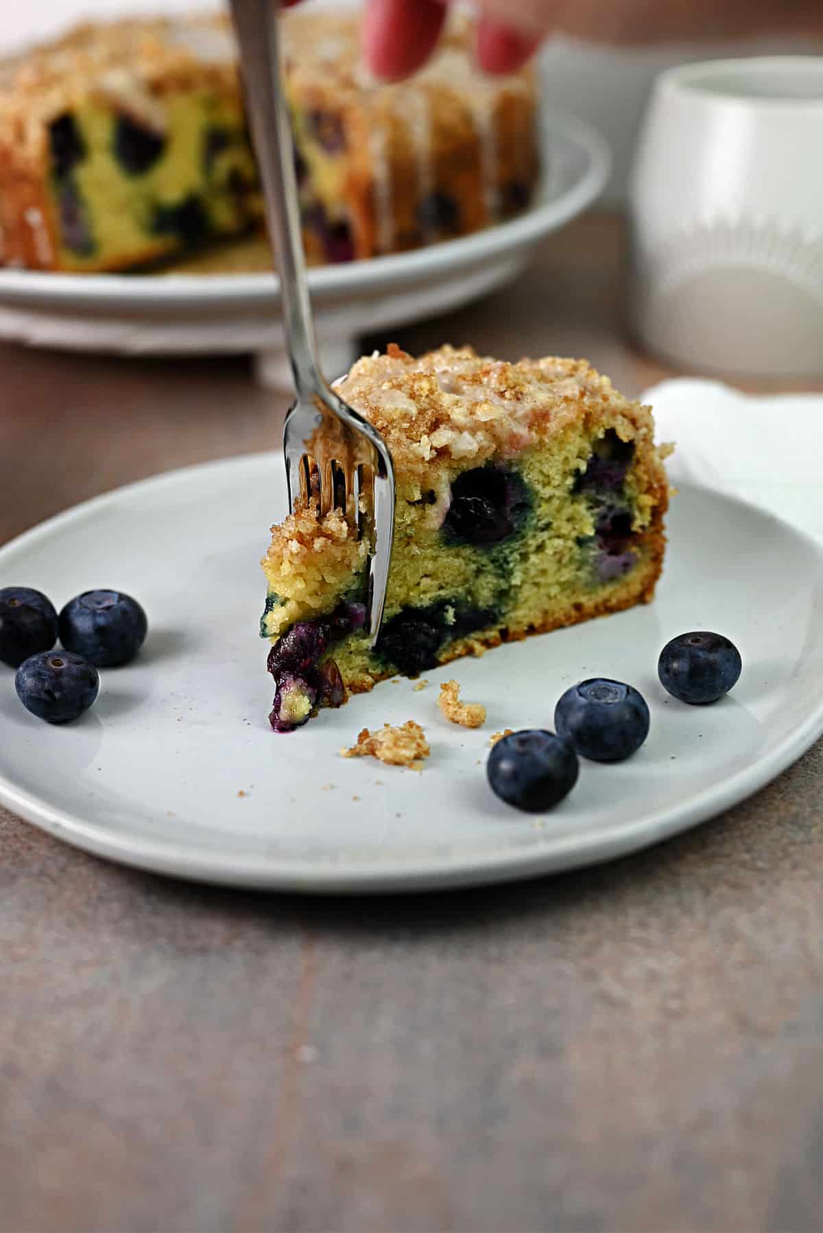 fork cutting into the slice of blueberry sour cream coffee cake.