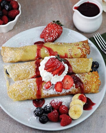 3 oat milk crepes rolled up with fruit and garnished with whipped cream and powdered sugar.