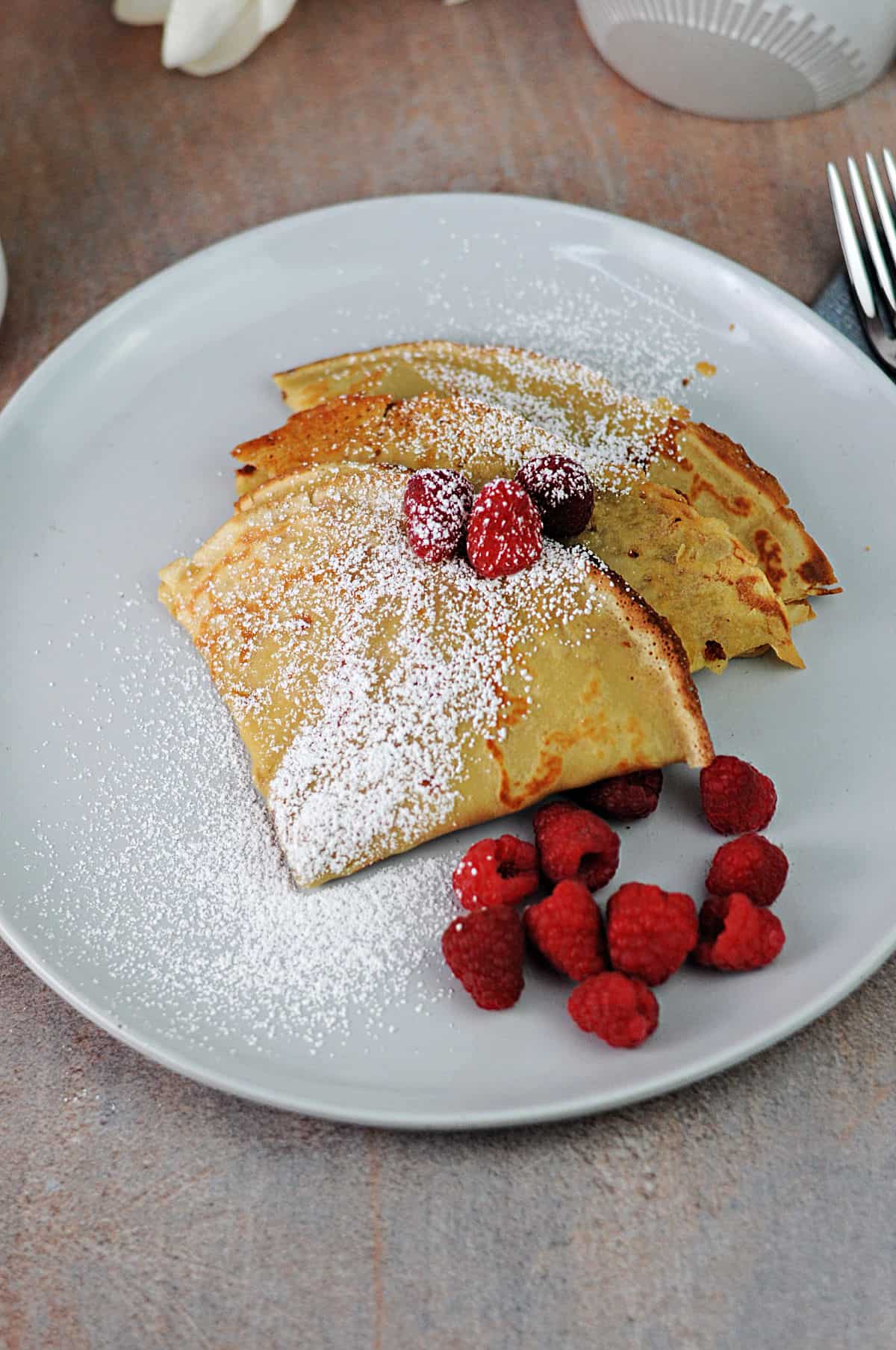 3 folded up oat milk crepes dusted with powdered sugar.