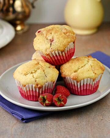 3 raspberry white chocolate muffins on a small plate, ready to eat.