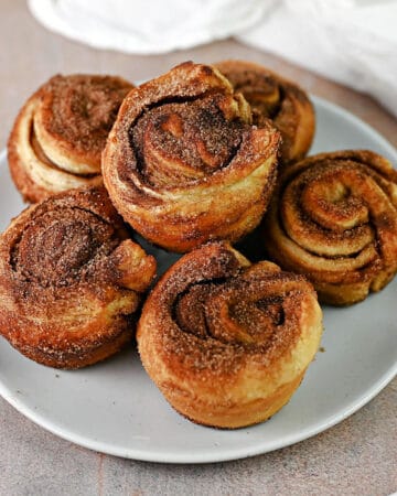 6 cinnamon roll puff pastry cruffins stacked on a small plate.