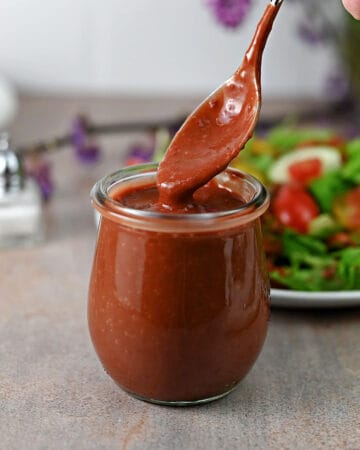 A spoon dripping strawberry balsamic vinaigrette dressing into a small jar.