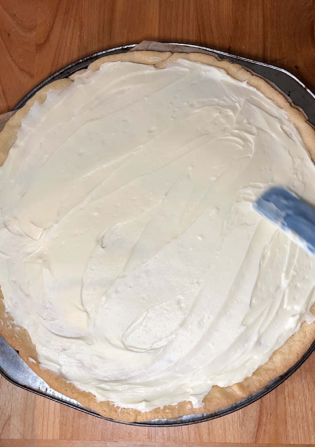 Spreading the cream cheese mixture on the cooled crust.