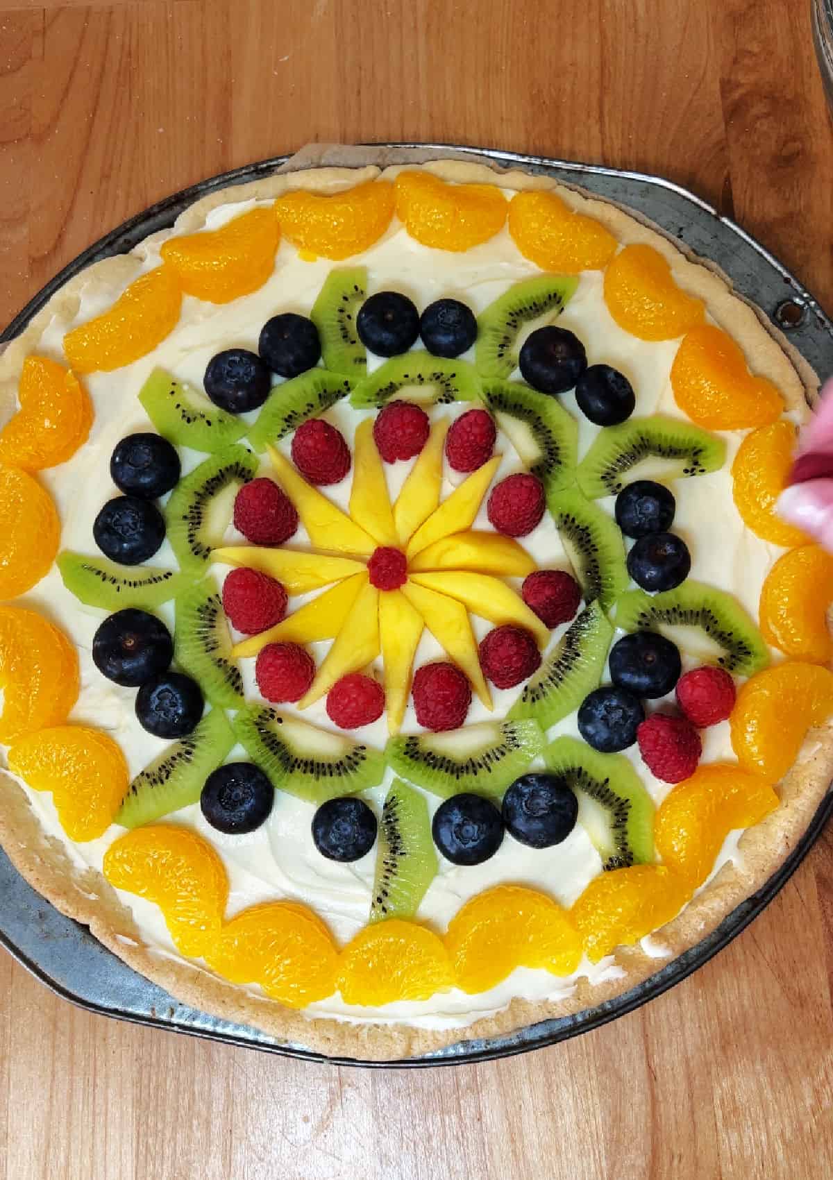 Decorating the fruit pizza with an arrangement of berries, kiwi, and mandarin oranges.