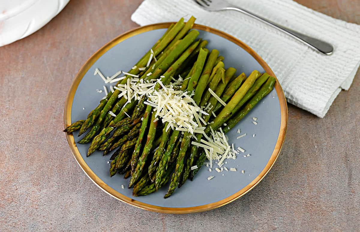 Plate of asparagus that was cooked in foil, sprinkled with shredded Parmesan cheese.
