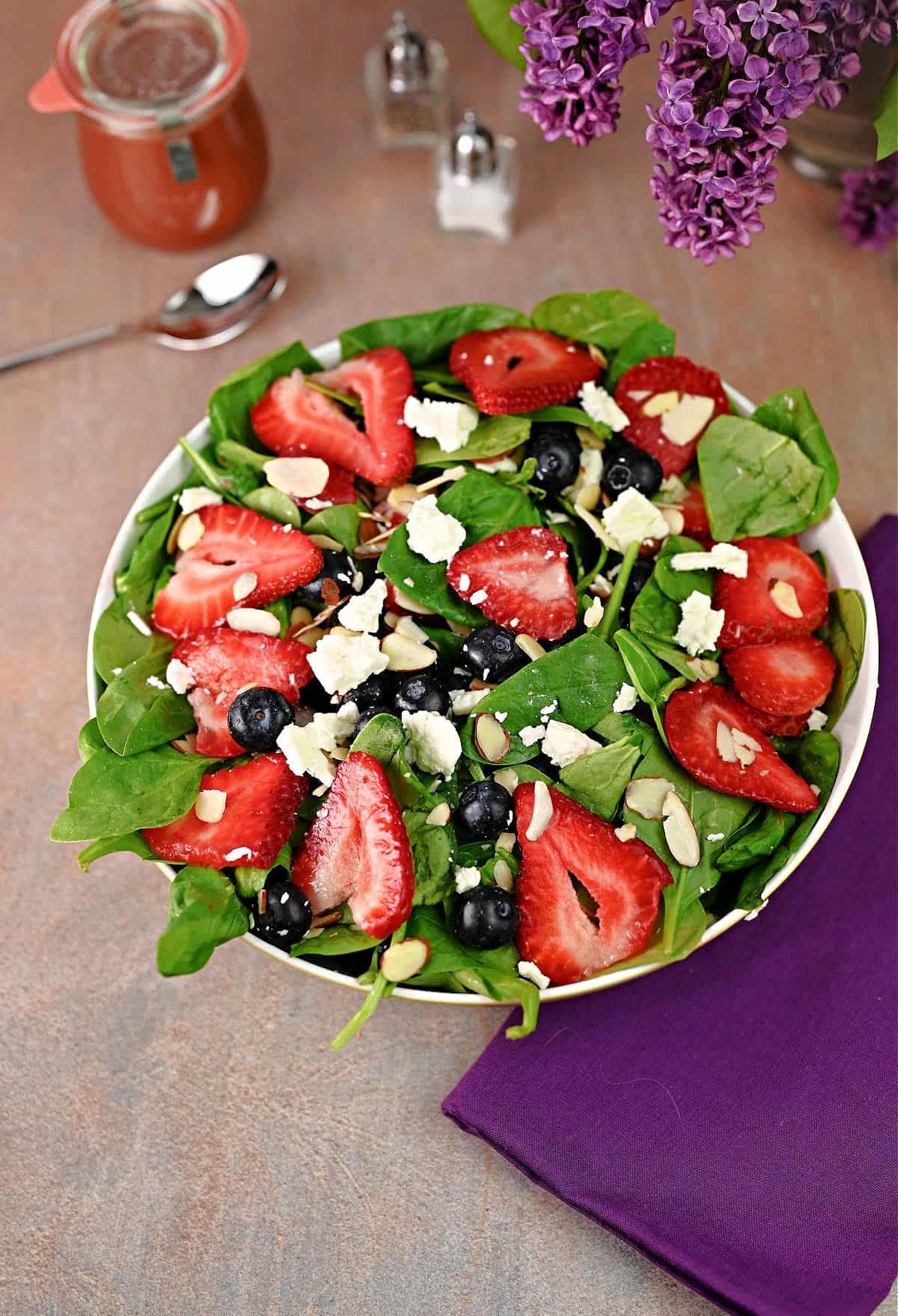 Spinach salad ready to serve with  jar of strawberry balsamic dressing nearby, ready to use.