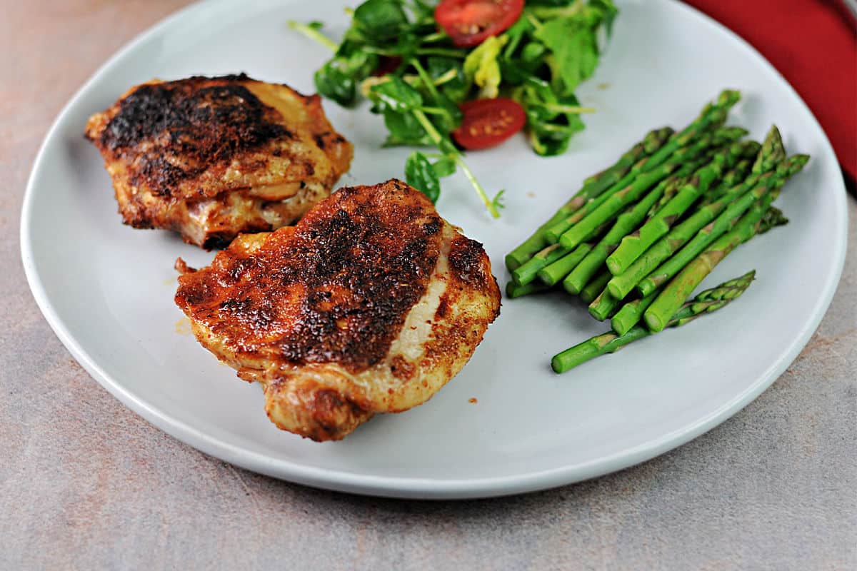 plate of chicken thighs served with a side of asparagus and a green salad.