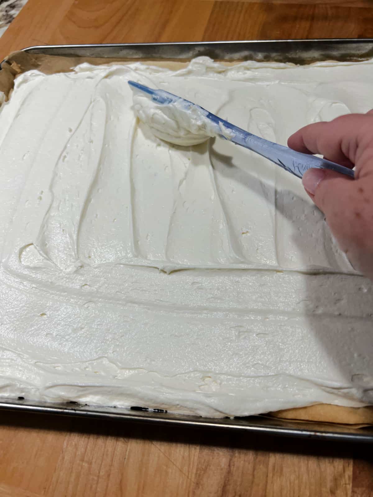 spreading the cream cheese frosting on the cookie crust.