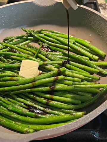 Sauteed asparagus being drizzled with balsamic vinegar.