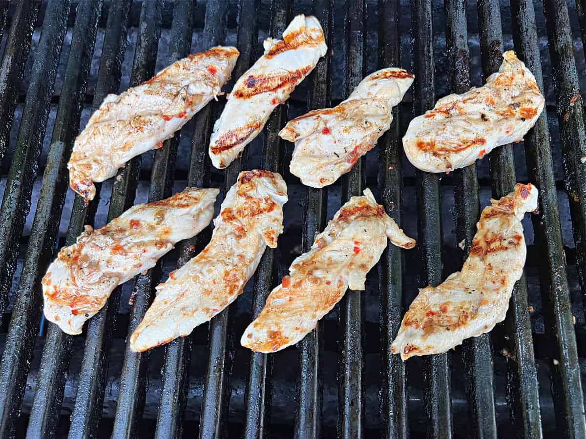 Chicken tenders cooking on a grill.