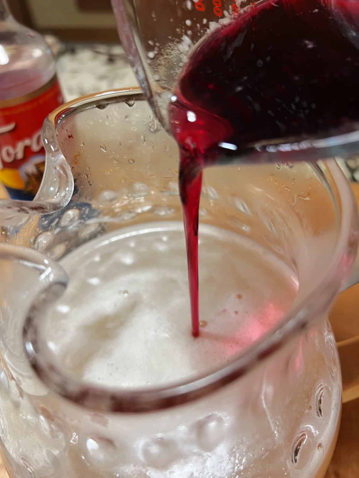 adding prickly pear syrup to the pitcher of lemonade.