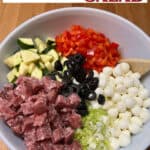 Pin showing salami pasta salad ingredients ready to be mixed in a bowl.
