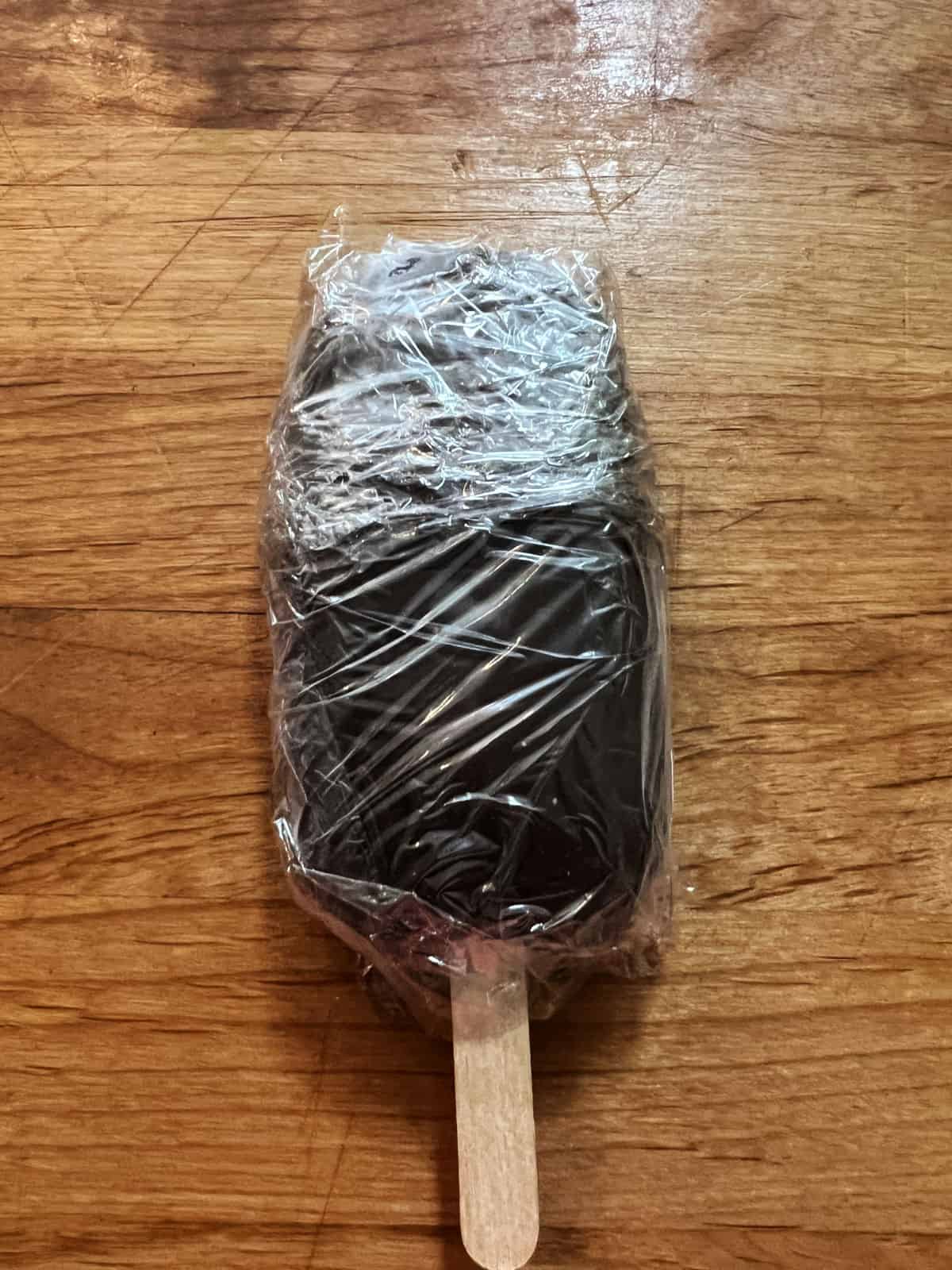 Homemade fudgesicle removed from mold and wrapped in plastic wrap.