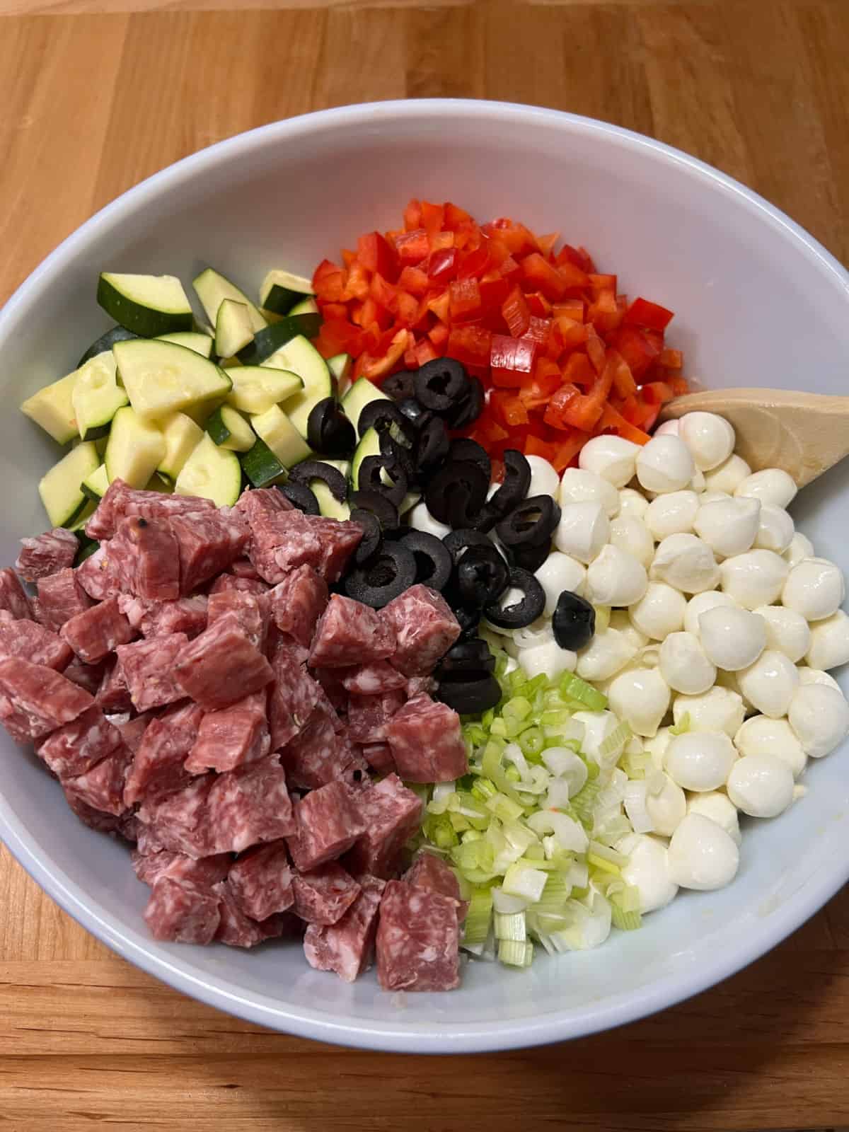 All ingredients added to bowl with pasta and dressing: salami, zucchini, bell pepper, olives, cheese, and green onions.