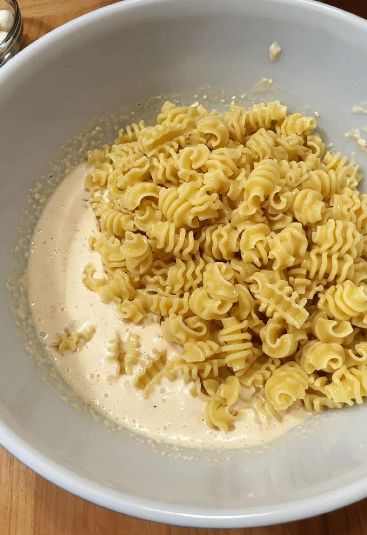 Adding cooked pasta to the bowl with dressing.