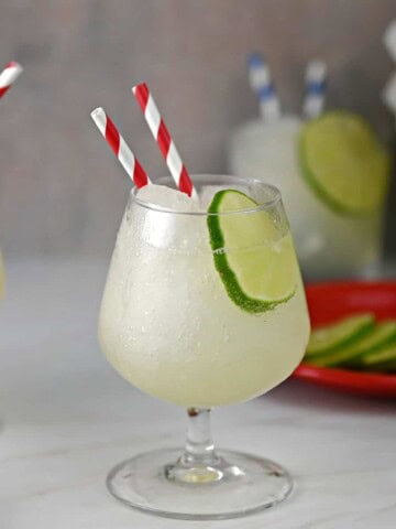 Frozen Daiquiri slush in a stemmed cocktail glass, garnished with a lime wheel, with striped straws for drinking.