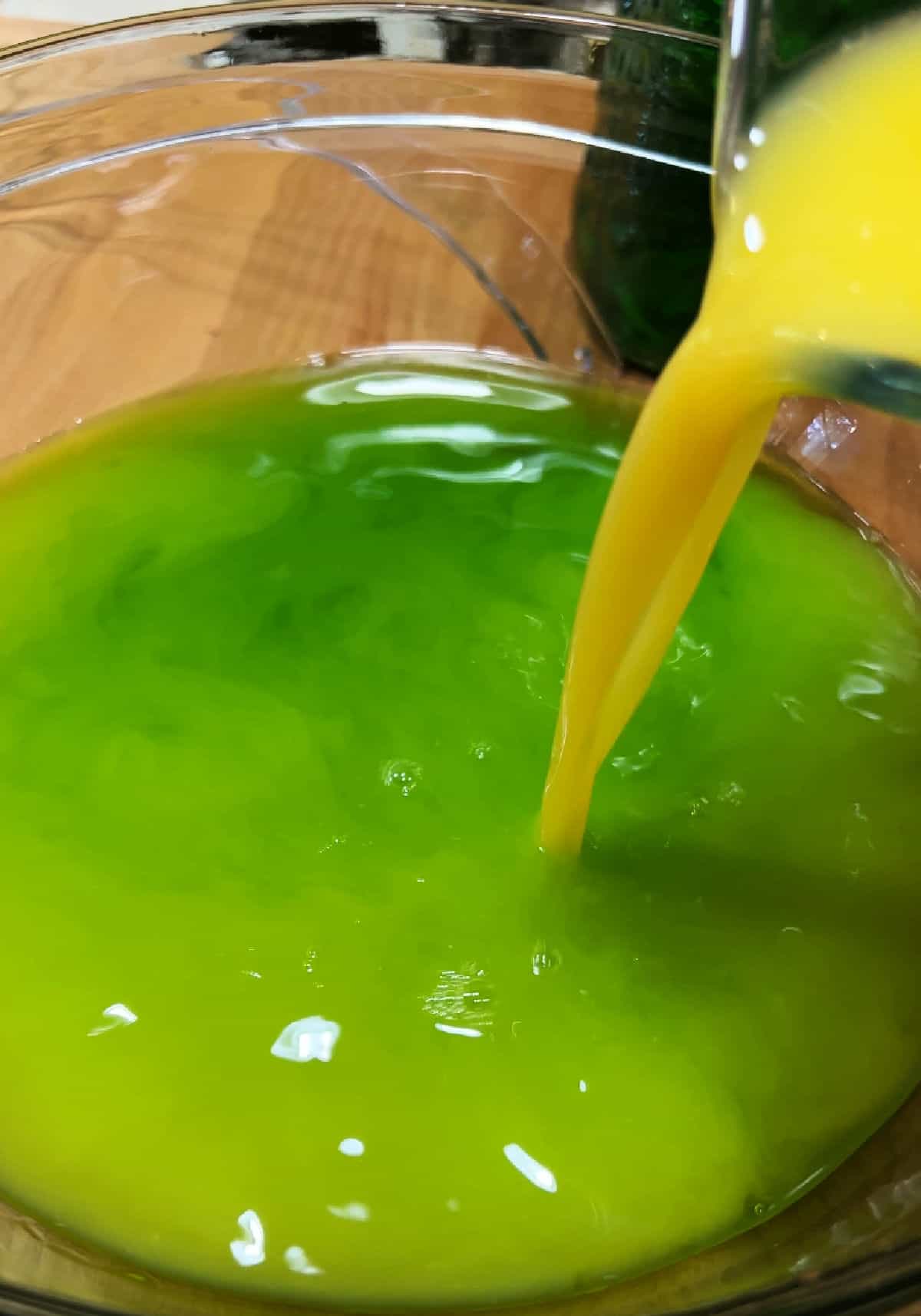 Adding orange juice to the green liqueur in the bowl.