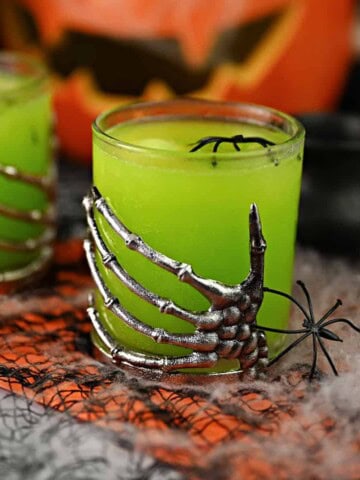 A skeleton hand decorated glass filled with yellow-green witches brew cocktail punch.