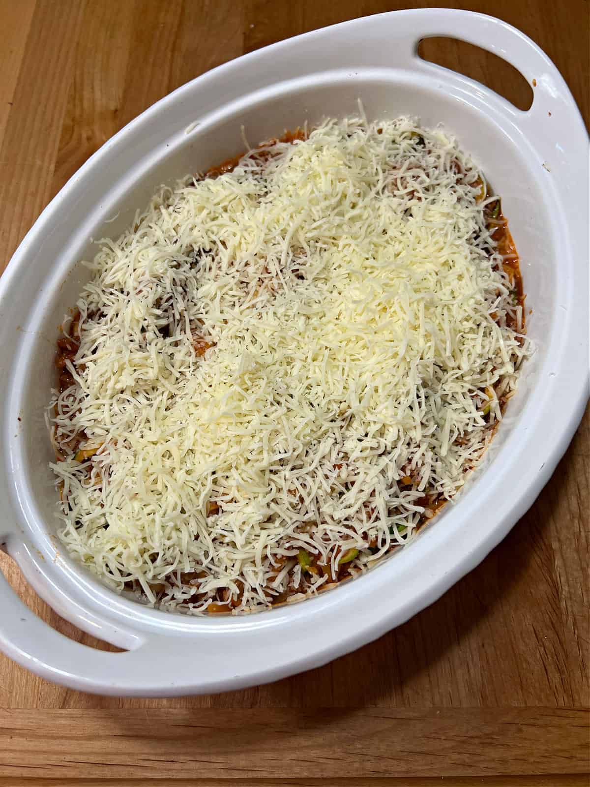 Mixture placed in a casserole dish with shredded cheese on top.