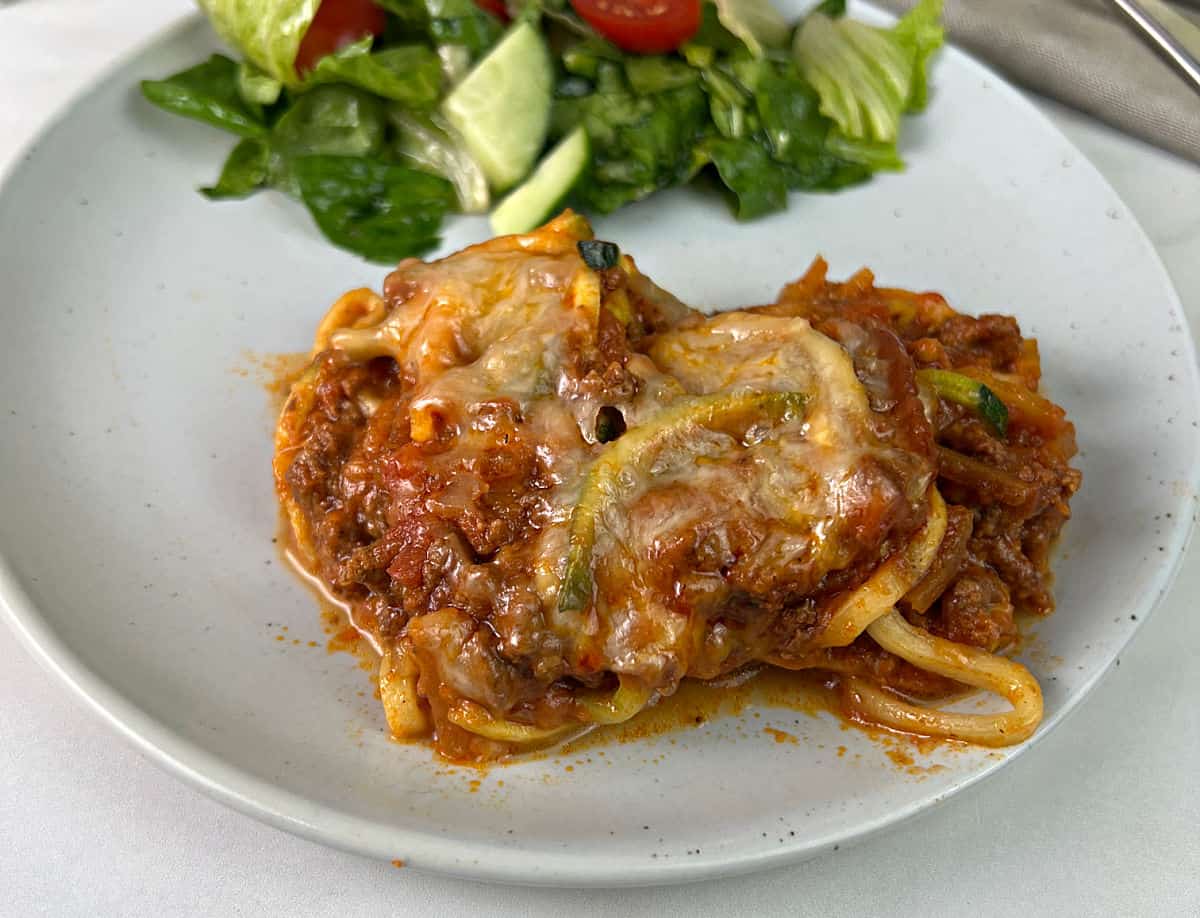 A serving of butternut squash and zucchini spaghetti bake on a plate with salad.