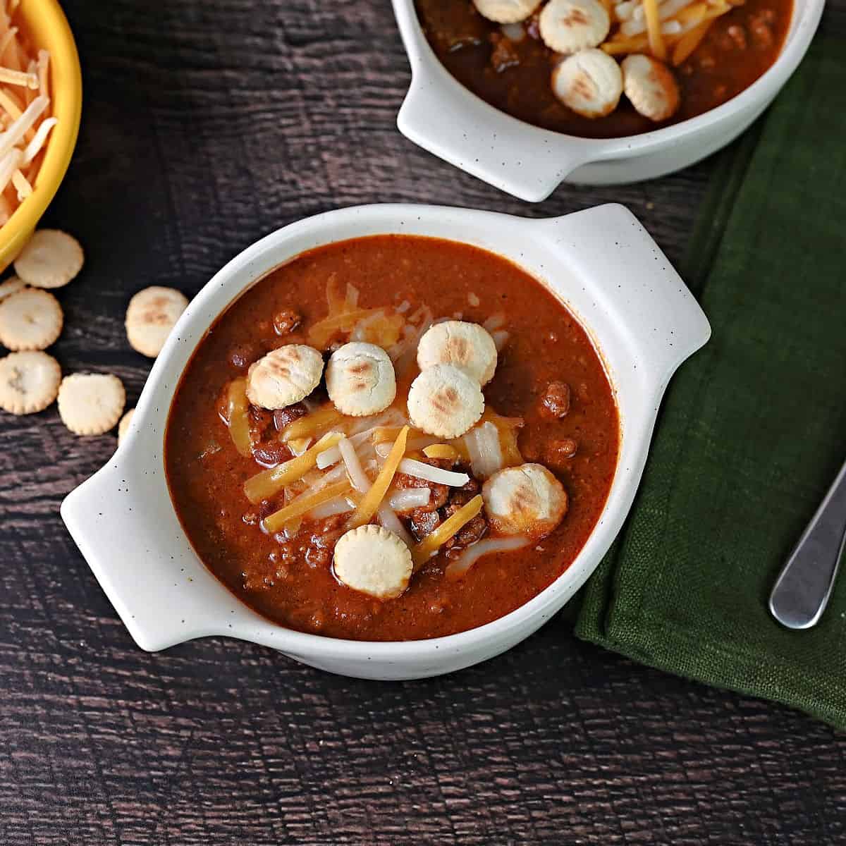 a bowl of old fashioned chili garnished with shredded cheese and oyster crackers.