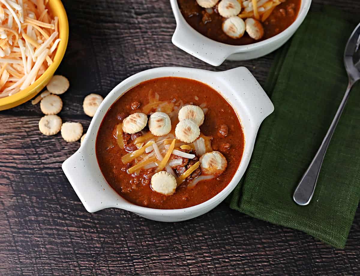 bowl of old fashioned chili garnished with shredded cheese and crackers.