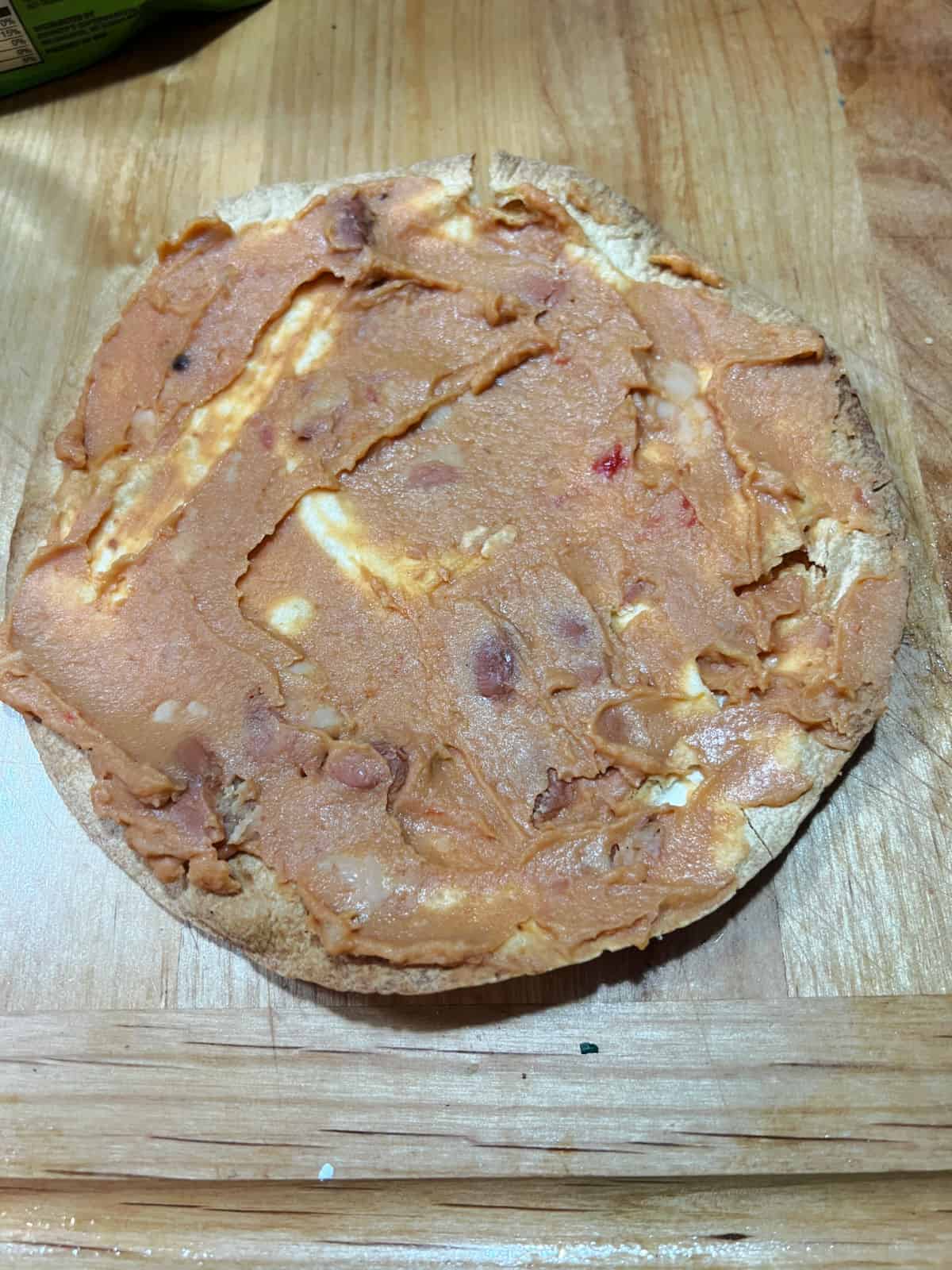 Cooked tortilla spread with a layer of refried beans.