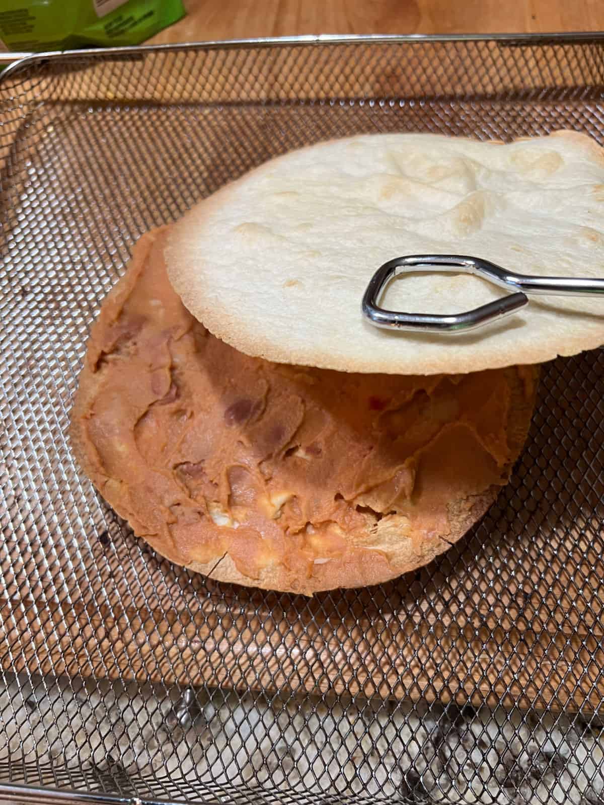 layering the second tortilla over the refried beans.