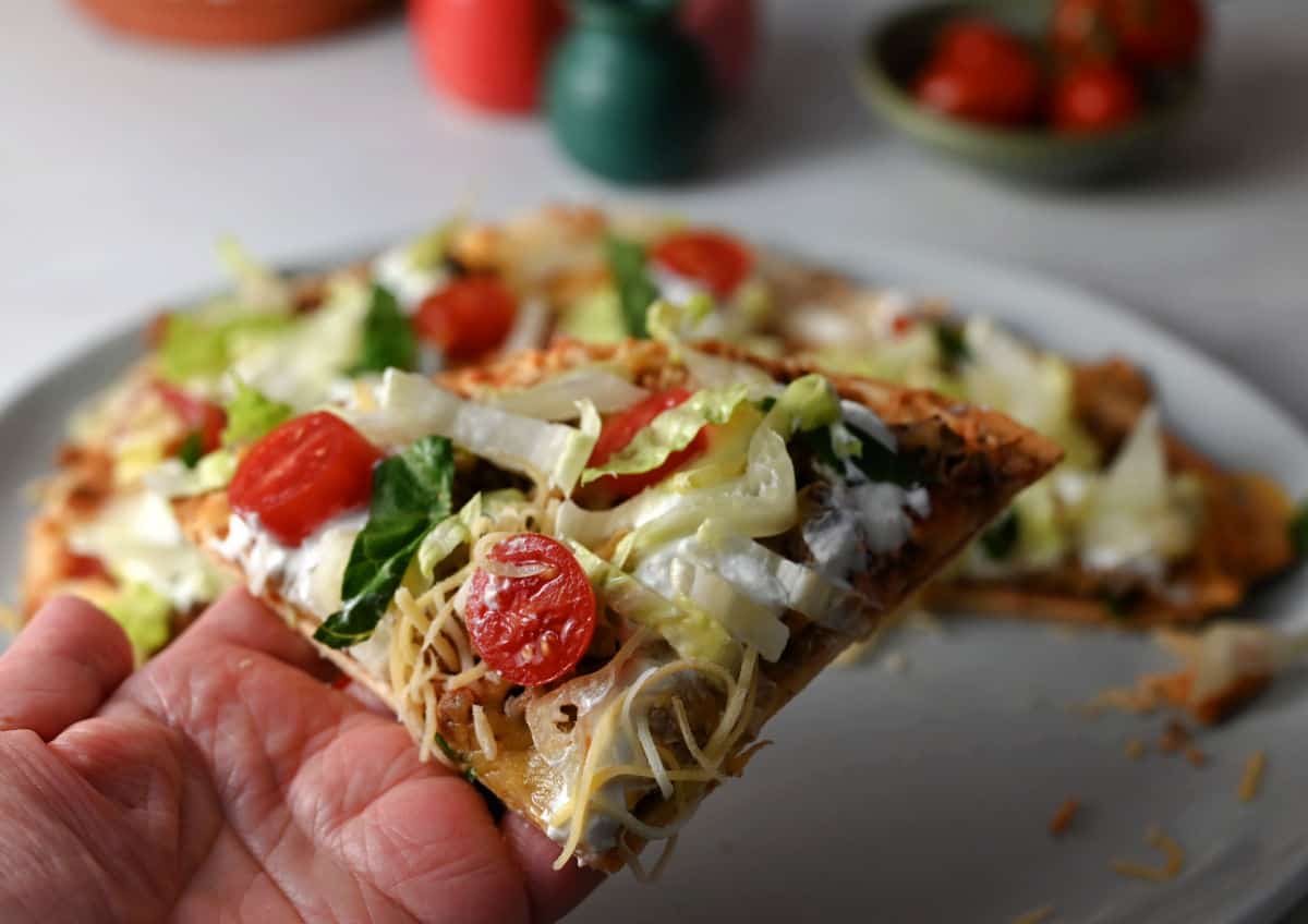 Close up of a hand holding a wedge of air fryer Mexican pizza.