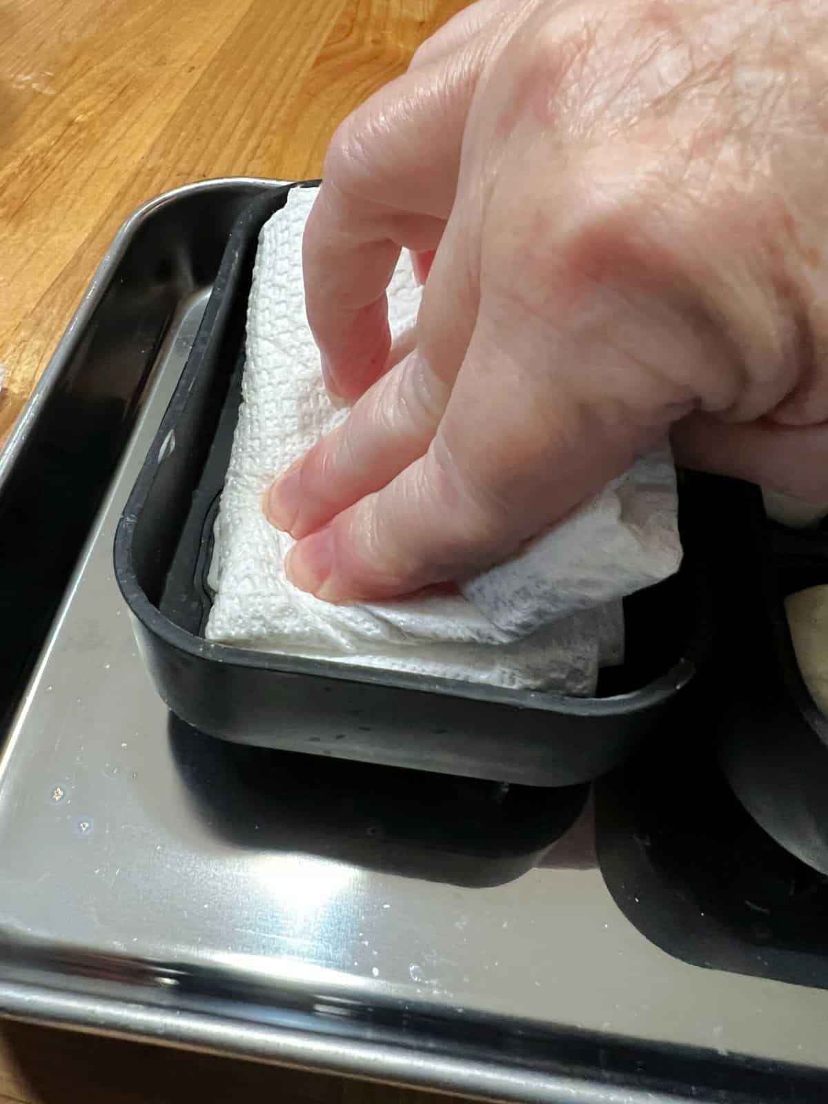 Using a paper towel to press the softened cheese into the mold.