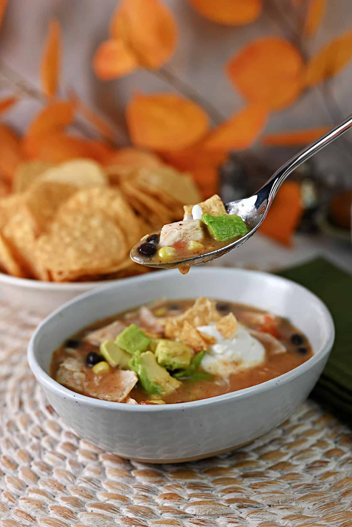 Spoon holding some soup suspended over the bowl of chicken tortilla soup.