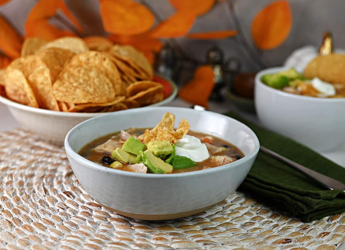 Bowl of chicken soup with tortilla chips crushed and added.