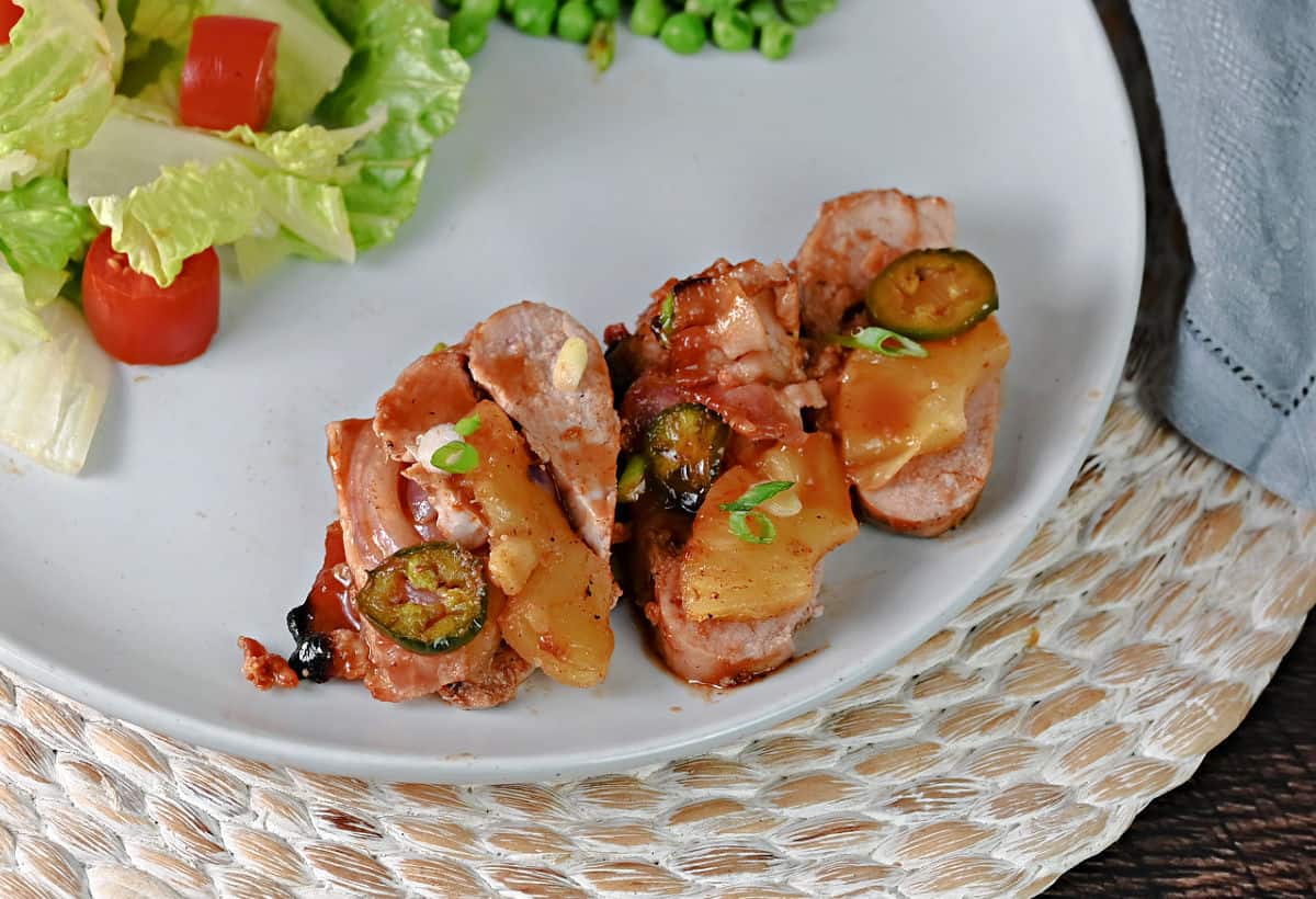 3 slices of hasselback pork on a plate with salad.