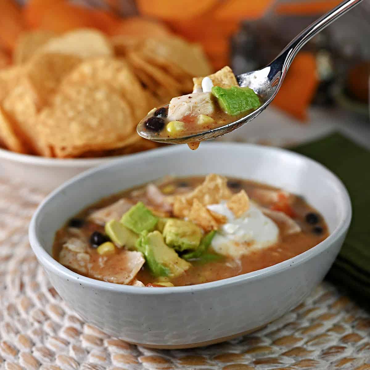 Spoon full of chicken tortilla soup suspended over a bowl with more soup.